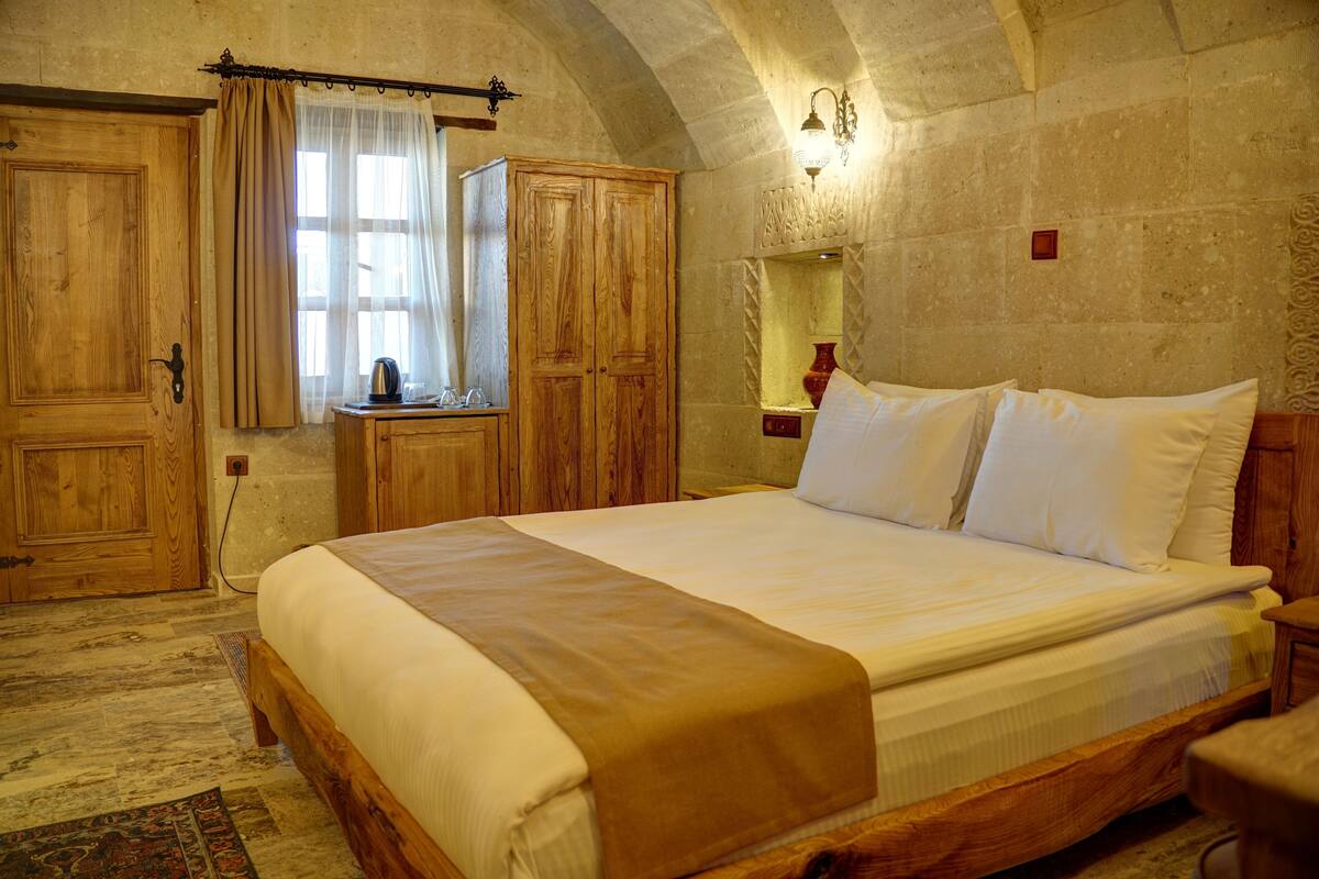 A bedroom with a large bed, wooden wardrobe, and a stone wall.