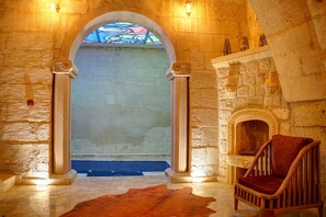 A stone-walled room with a stone fireplace, a wooden chair, and a blue tiled area. - The Calypso Cave (Ürgüp)