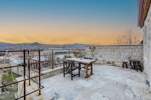 A rooftop terrace with a table and chairs, a stone wall, and a view of distant mountains. - The Calypso Cave (Ürgüp)