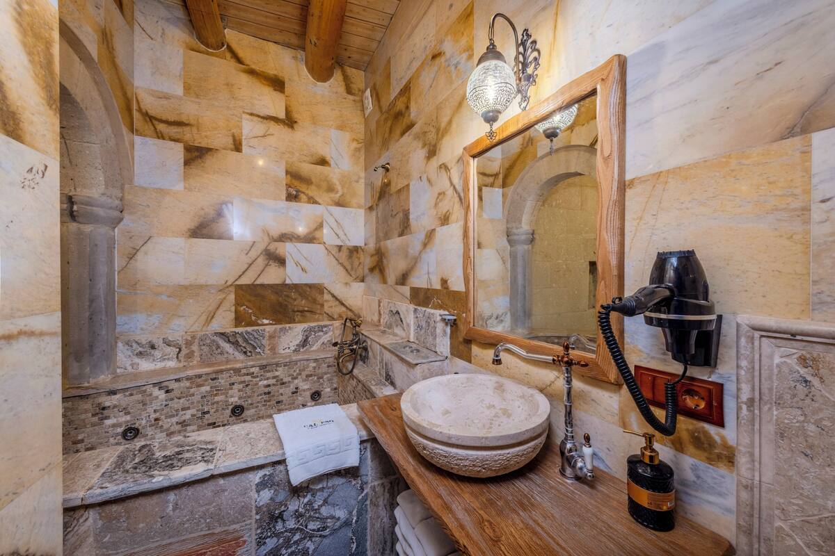A bathroom with a stone wall, a wooden vanity, a round sink, a mirror, a towel, and a hairdryer.