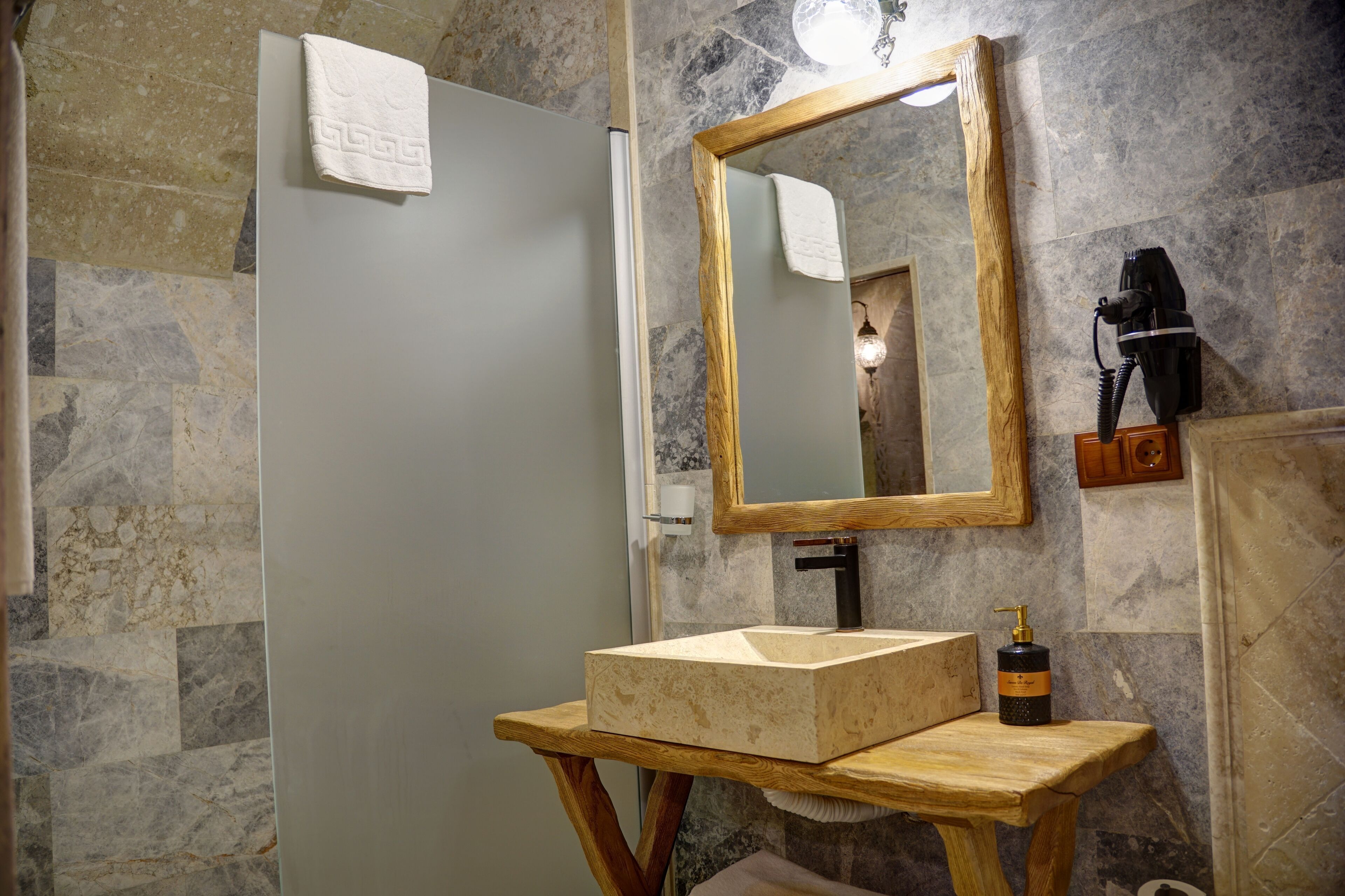 A bathroom with a marble wall, a wooden vanity, a large mirror, and a towel hanging on the door.