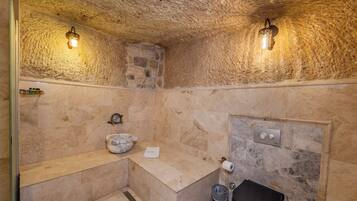Un baño con paredes de piedra, un lavamanos de mármol, un cubo de basura negro y una toalla sobre el mostrador.