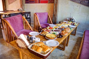 A dining table set with various dishes, bread, and drinks, surrounded by wooden chairs. - The Calypso Cave (Ürgüp)
