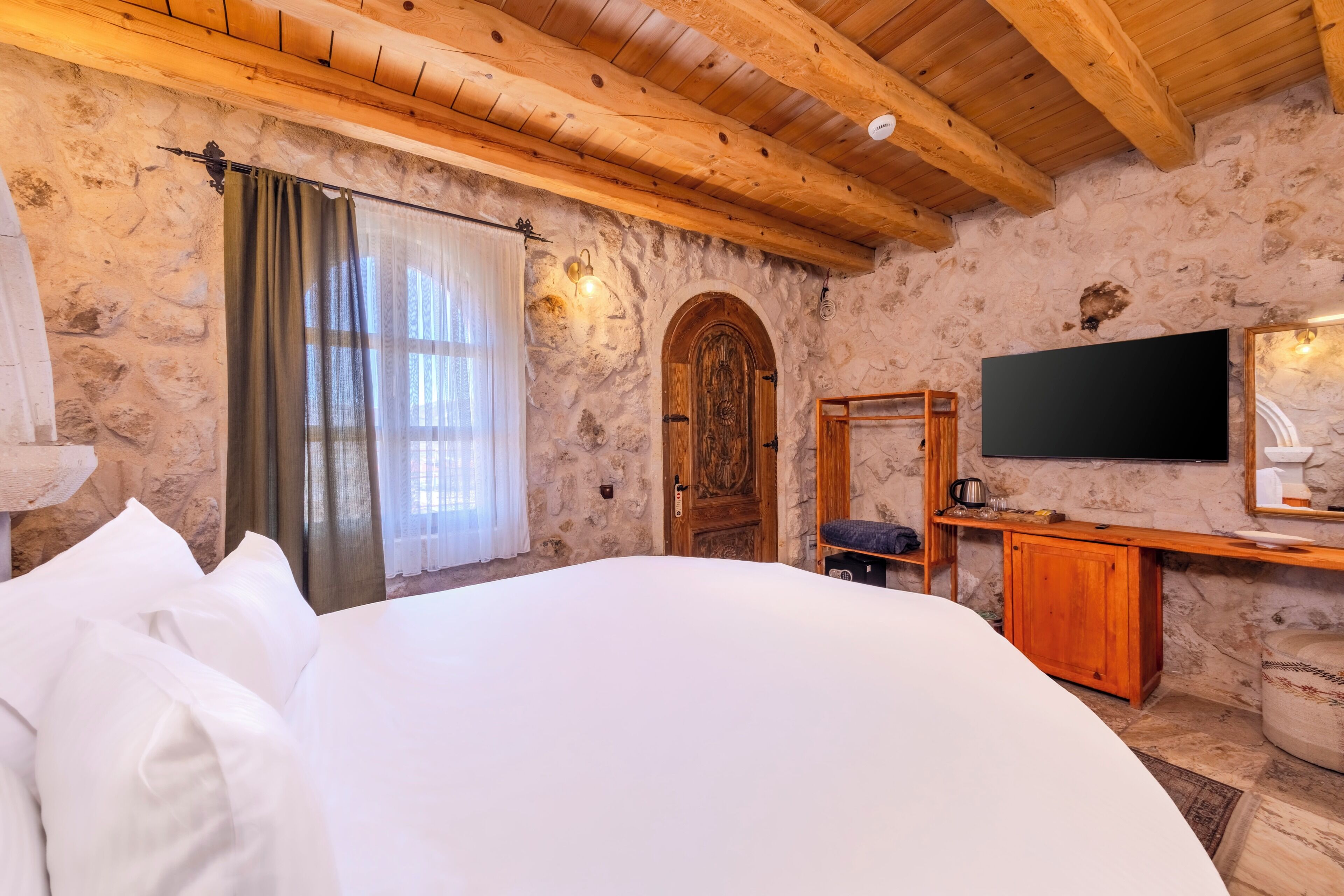 Une chambre avec un grand lit, des murs en pierre, des poutres en bois, une télévision et une cheminée en pierre.