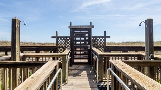 A wooden boardwalk leading to a gated entrance with a lattice structure. - One Bedroom, One Bathroom Condo on the Oceanside (Carolina Beach)
