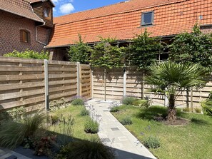 A brick house with a tiled roof, a wooden fence, and a garden with various plants and a pathway.