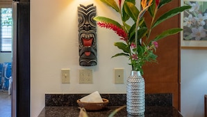 A modern kitchen with a marble countertop, a decorative vase with flowers, a wall-mounted light fixture, and a wooden door.