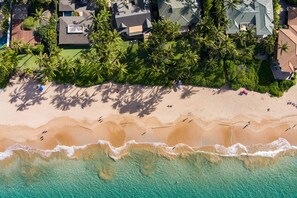 An aerial view of a beachfront property with a sandy beach, clear turquoise waters, and a cluster of palm trees. - NEW LISTING Private Home across from Keawakapu Beach Tennis Pickleball Court! (Kihei)