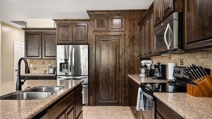 A modern kitchen with dark wooden cabinets, stainless steel appliances, granite countertops, and a built-in oven. - DUNE-OUR-THING, PRIVATE POOL, BBQ, BASKETBALL, PUTTING GREEN, SAND HOLLOW (Hurricane)