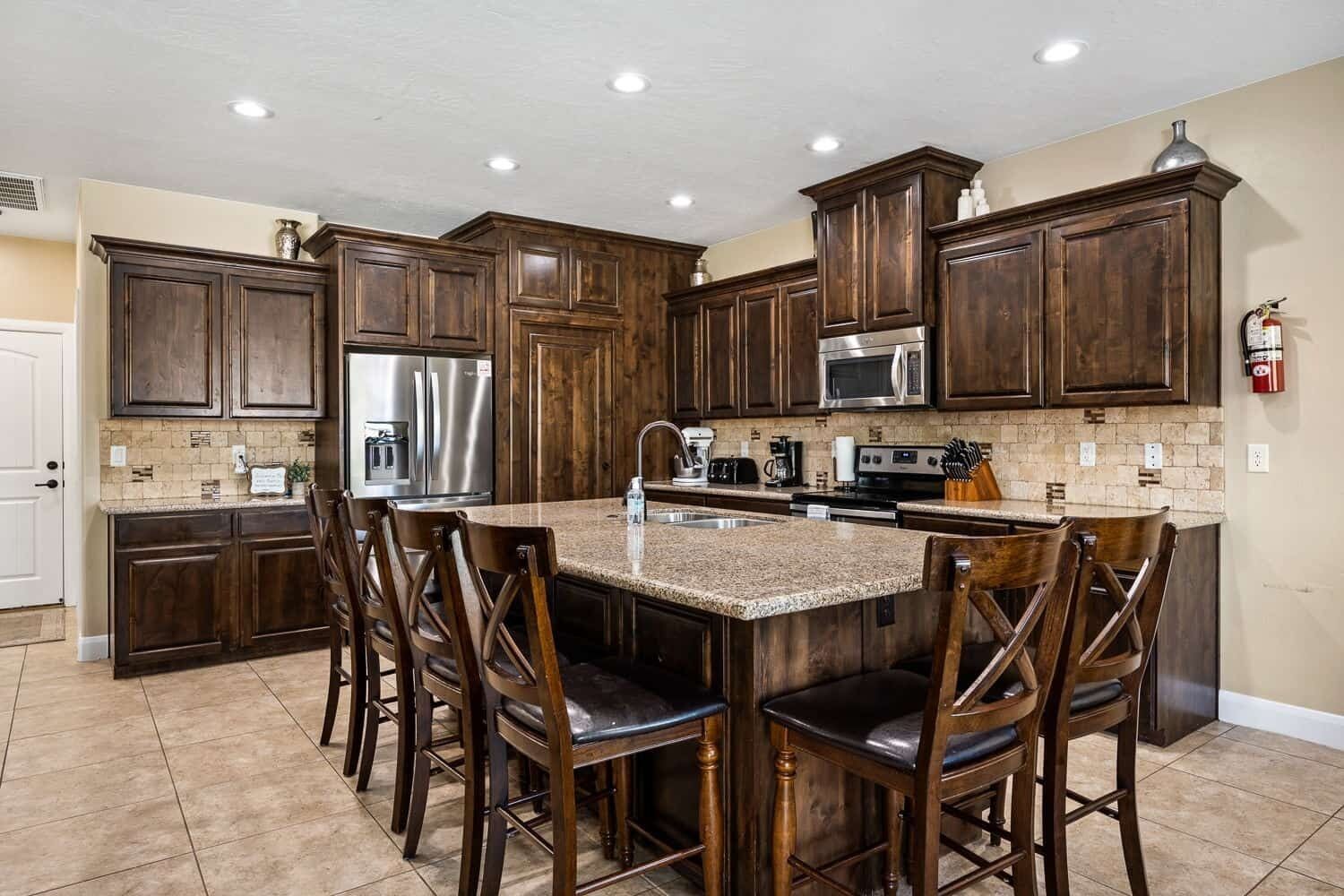 A kitchen with dark wooden cabinets, a stainless steel refrigerator, a microwave, and a granite countertop.