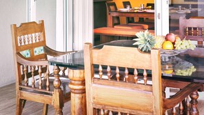 Een eetgedeelte met een houten tafel en stoelen, een tafel met een glazen blad en een schaal fruit op de tafel.