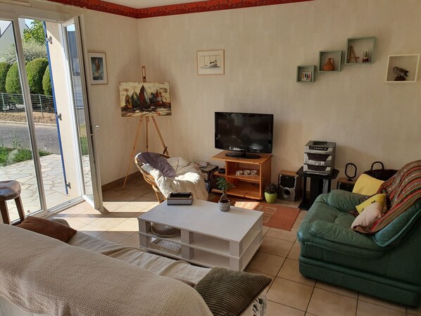 A living room with a sofa, a green armchair, a coffee table, a TV on a wooden stand, and a painting on the wall.