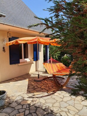 A patio area with a hammock, striped umbrellas, and a stone-tiled floor.