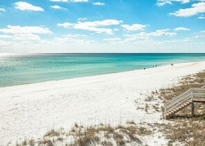 A beach with a wooden staircase leading down to the sand, clear turquoise water, and a clear sky.