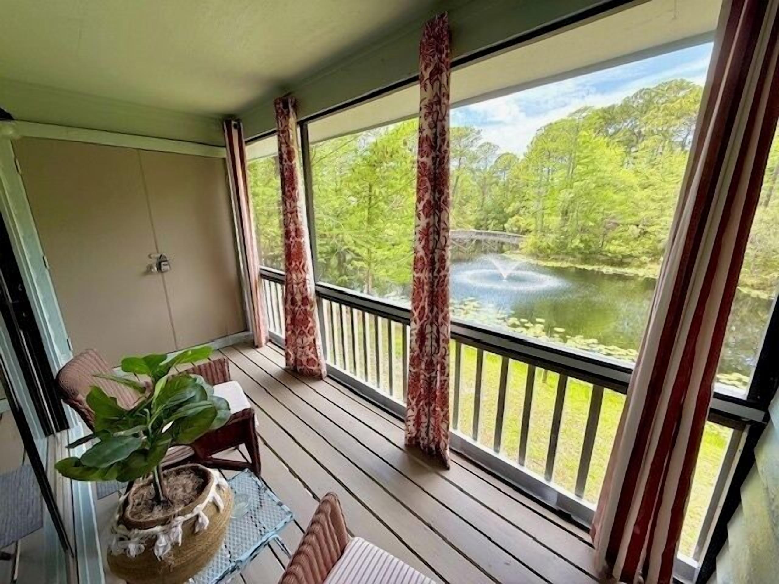 A covered porch with a view of a pond and trees.