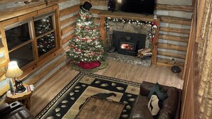 En mysig timmerstuga med en öppen spis, en julgran, en tv och en soffa klädd i läder.