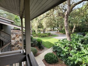 A covered porch with a stone wall, a staircase, and a view of a well-maintained lawn and trees. - Modern/Elegant (Haines City)