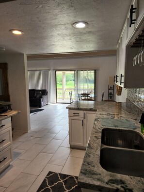 A modern kitchen with white cabinets, a granite countertop, and a large island. There is a sliding glass door leading to a patio with a dining table and chairs. - Modern/Elegant (Haines City)