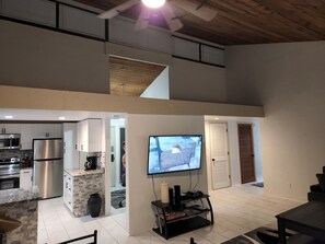 A modern kitchen with stainless steel appliances, a dining area with a TV, and a loft space with a wooden ceiling. - Modern/Elegant (Haines City)