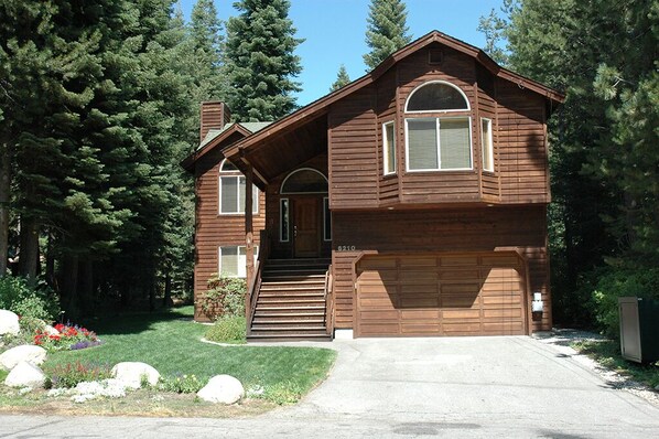 Stunning cabin with a central entrance, flanked by two windows, set amidst a beautifully manicured lawn and surrounded by tall evergreen trees.
