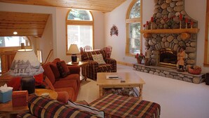 Un salon chaleureux avec une cheminée en pierre, un plafond en bois et de grandes fenêtres.