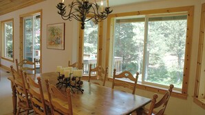 Une salle à manger avec une table et des chaises en bois, de grandes fenêtres et un lustre.