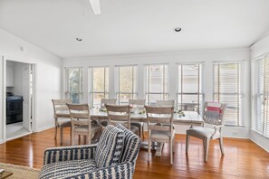 Ein geräumiges Wohnzimmer mit Essbereich, großen Fenstern mit Jalousien und Holzböden.