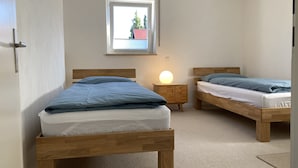 A bedroom with two wooden beds, a nightstand with a lamp, and a window with a view of trees and a building.