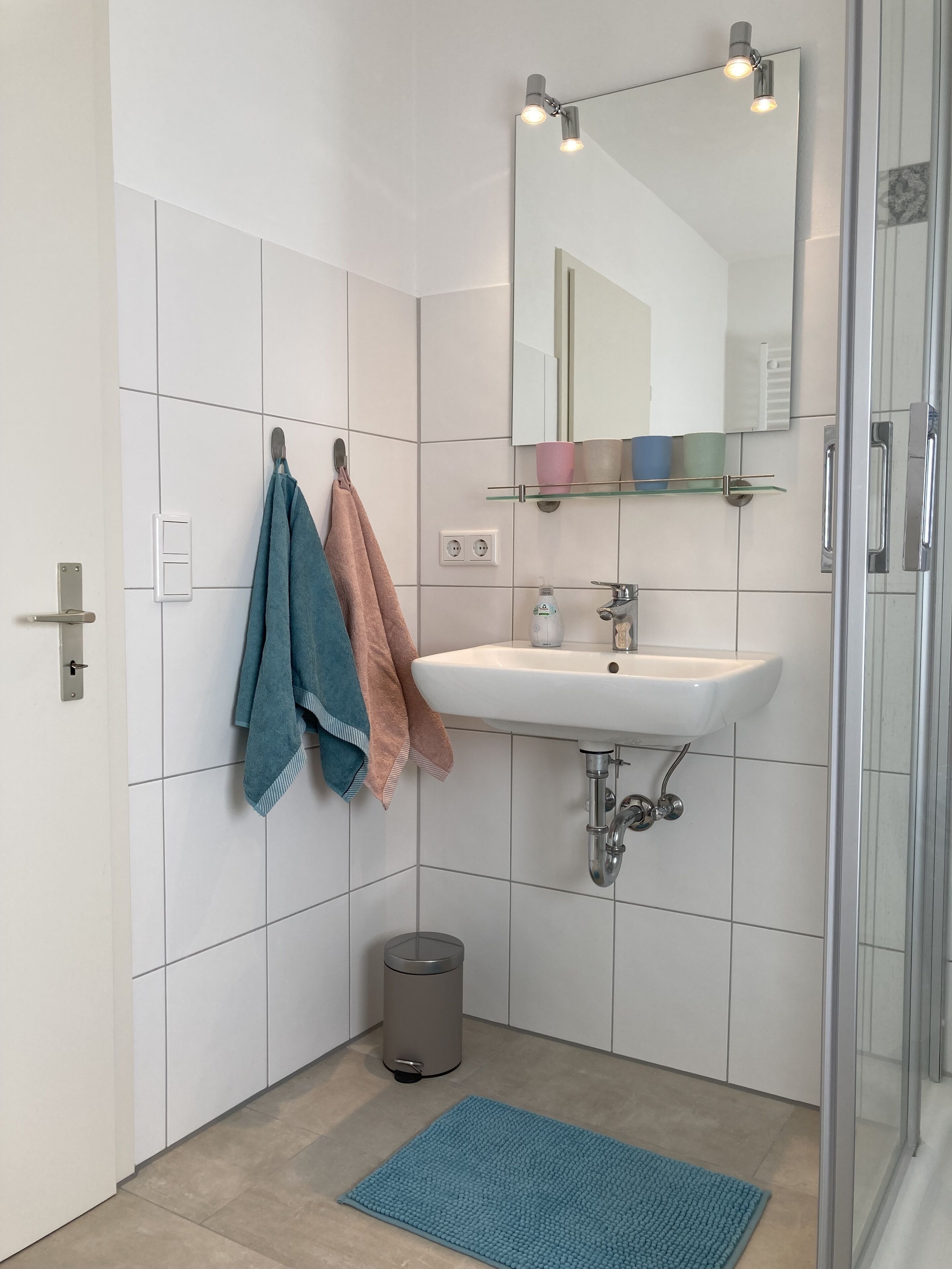 Ein modernes Badezimmer mit weißen Fliesen, einem Waschbecken, einem Spiegel und einer Glasdusche.