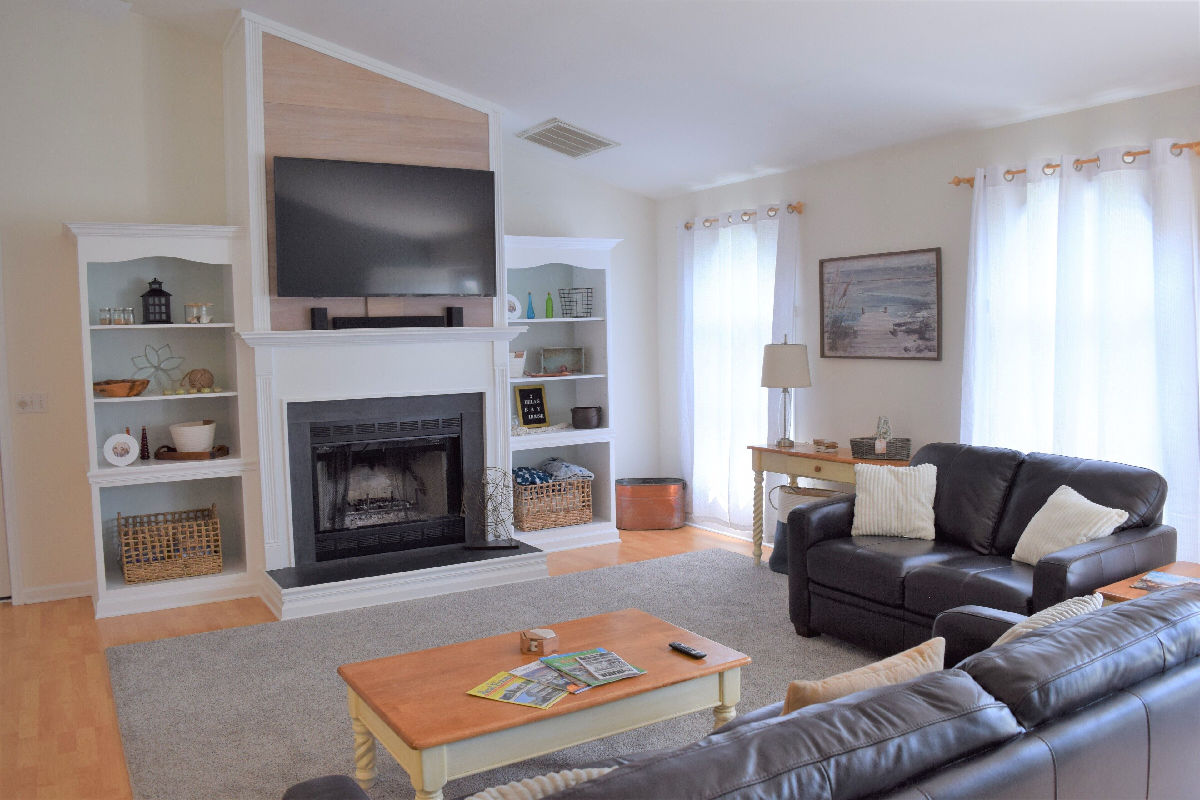 A living room with a fireplace, a black leather sofa, a wooden coffee table, and a television mounted above the fireplace.