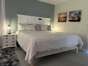 A bedroom with a bed, nightstands, a lamp, a fluffy rug, and two wall art pieces.