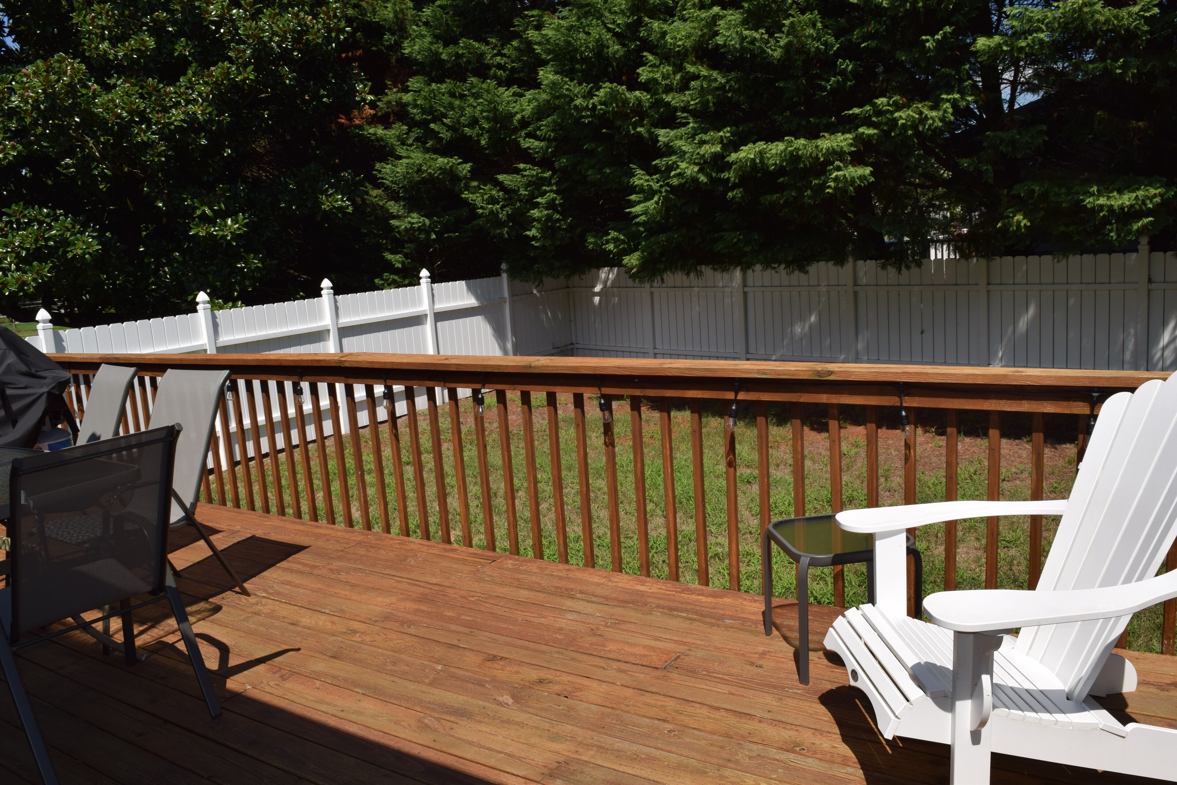 Una terraza de madera con valla blanca, una silla Adirondack blanca y una pequeña mesa.