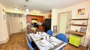 A modern kitchen with wooden cabinets, a black refrigerator, and a dining area with blue chairs and a table set for four. - World Cup-Ready! - Walk to MBS - Parking - ADA (Atlanta)