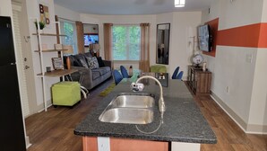 A compact living space with a kitchen area featuring a granite countertop and stainless steel sink. There is a sofa and a small dining table with chairs. - World Cup-Ready! - Walk to MBS - Parking - ADA (Atlanta)