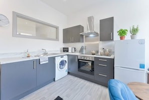 A modern kitchen with grey cabinets, a built-in oven, a microwave, and a washing machine.