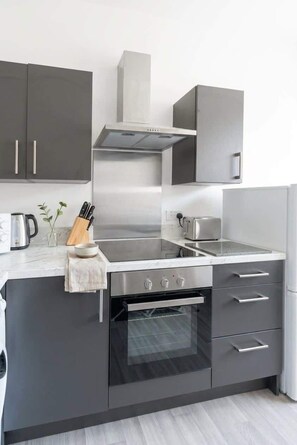 Una cucina moderna con elettrodomestici in acciaio inossidabile, forno integrato e un piano di lavoro con bollitore e utensili.