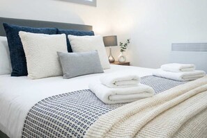 Un letto rifatto con cuscini, una lampada da comodino e asciugamani piegati.
