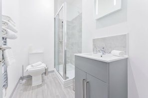 A modern bathroom with a glass-enclosed shower, a toilet, and a vanity with a mirror.