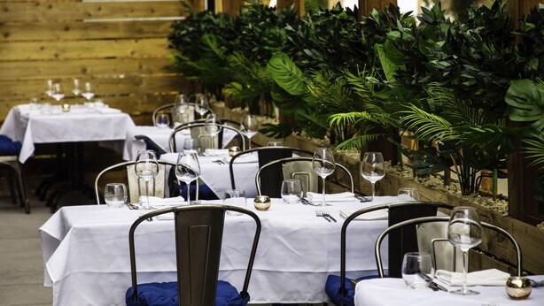 A restaurant with tables set for dining, featuring white tablecloths and metal chairs.