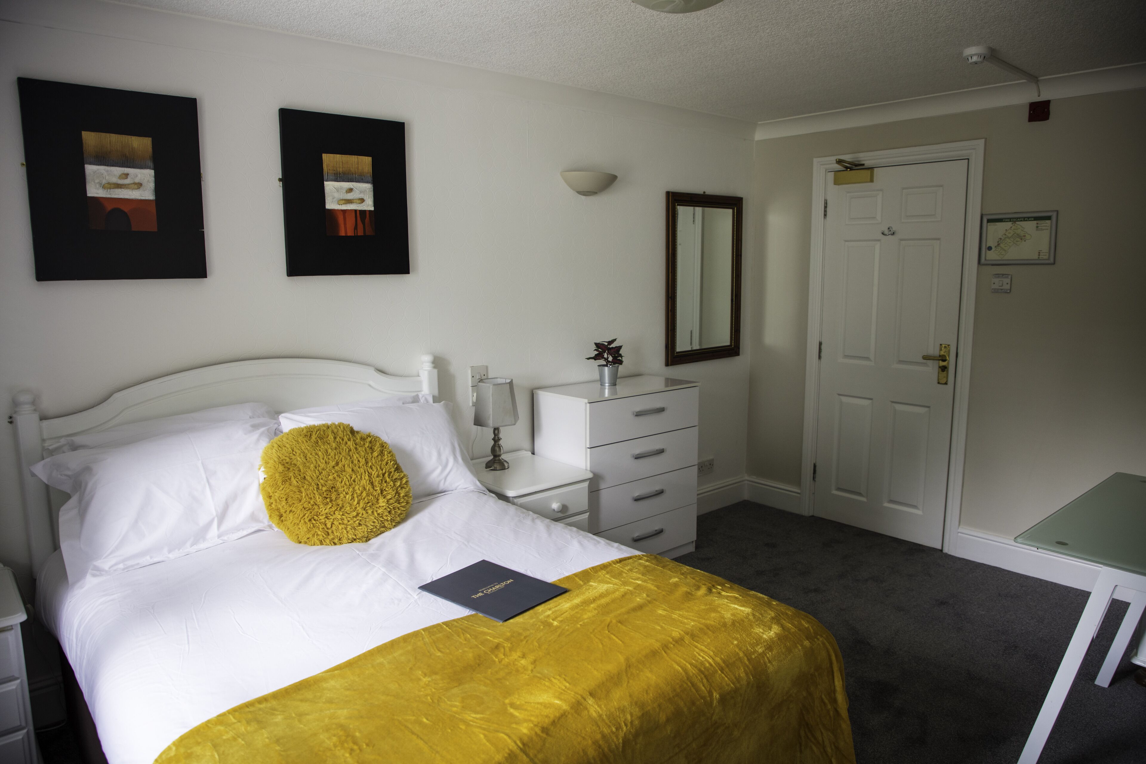 A neatly arranged bedroom with a bed, bedside tables, a dresser, a mirror, and a door.