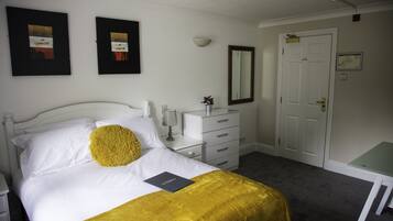 A neatly arranged bedroom with a bed, bedside tables, a dresser, a mirror, and a door.