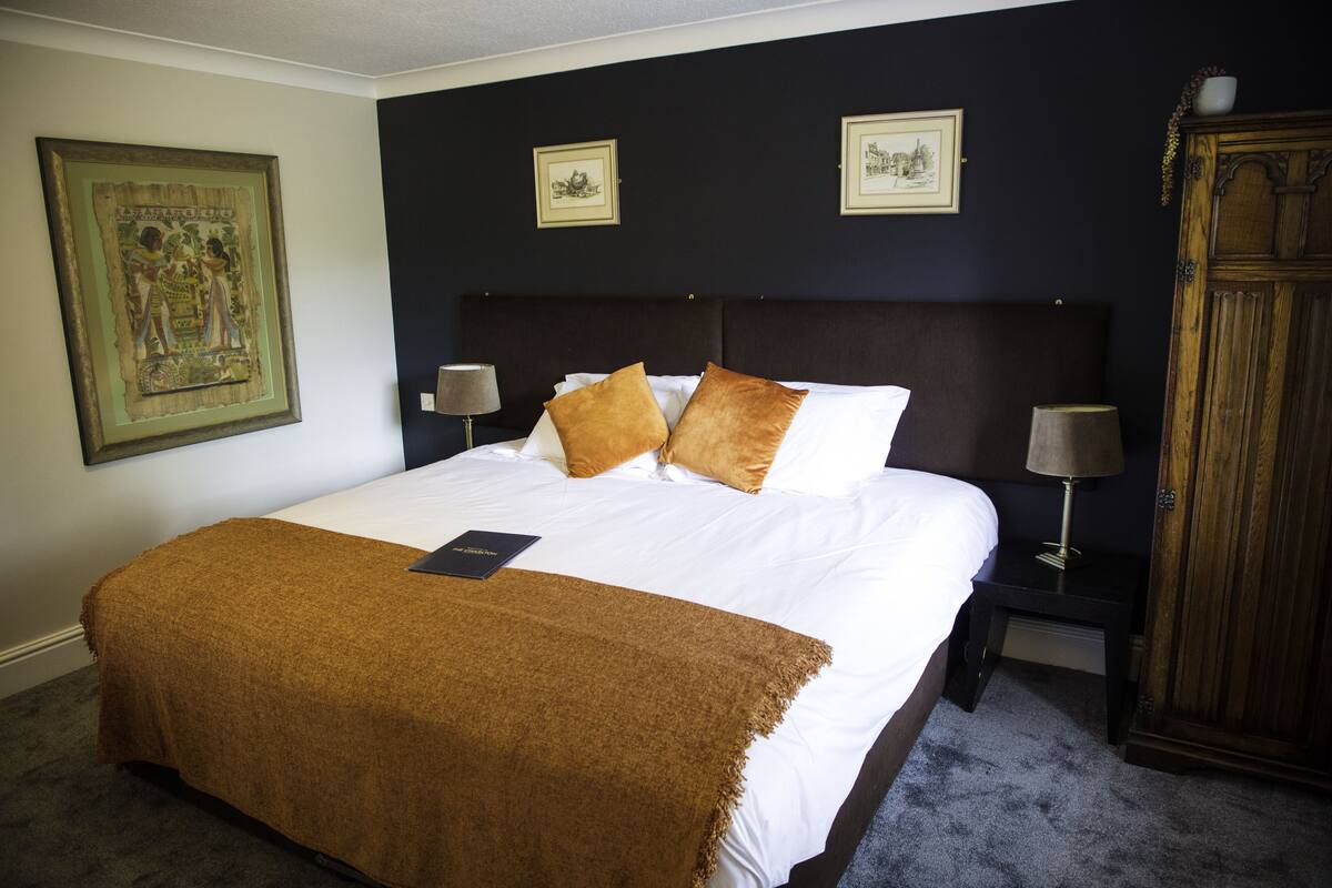 Ein Hotelzimmer mit einem großen Bett, zwei Nachttischlampen, einem Holzschrank und gerahmten Bildern an der Wand.
