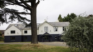 A two-story building with a dark and light facade, a prominent entrance, and a large tree in the foreground.