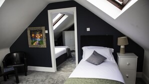 A bedroom with a skylight, a bed with a green throw, a nightstand, a chair, and a painting on the wall.