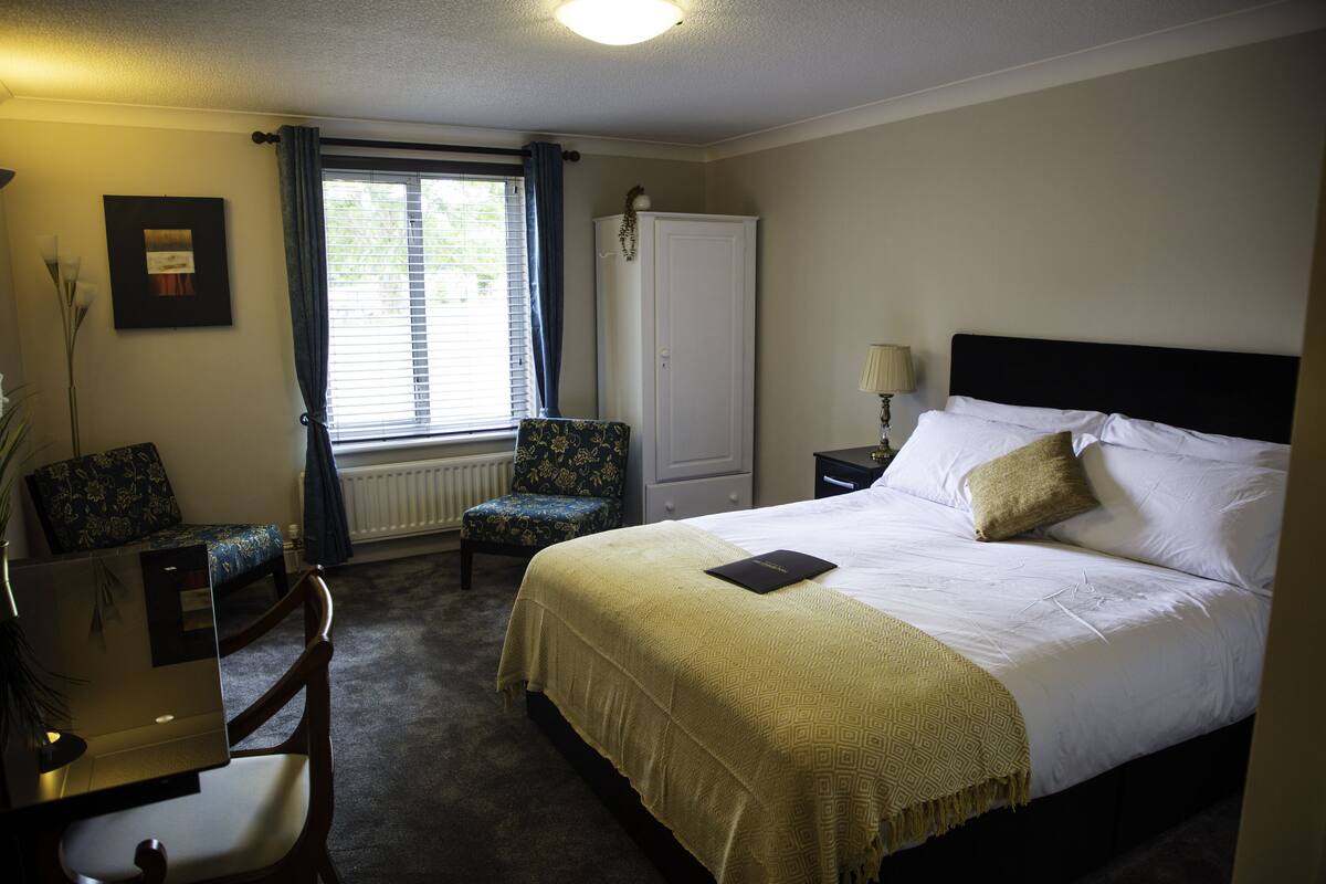 Ein Hotelzimmer mit einem Bett, einem Schreibtisch, einem Stuhl, einem Heizkörper und einem Fenster mit Vorhängen.