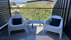 A balcony with two white chairs and a small table, overlooking a garden and buildings. - Luxury on Bayview Wifi Linen included (Inverloch)