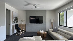 A modern living room with a sofa, a chair, a coffee table, a TV mounted on the wall, and a ceiling fan. - Luxury on Bayview Wifi Linen included (Inverloch)