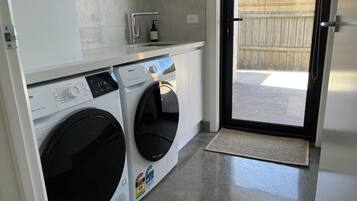 A compact laundry area with a front-loading washer and dryer, a small countertop with a soap dispenser, and a door leading to an outdoor area.