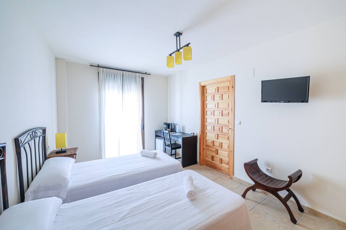 Habitación de hotel con dos camas, un escritorio, una silla, un televisor y una puerta de madera.