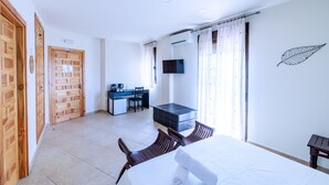 A hotel room with a bed, a desk, a chair, a small kitchenette, and a TV. - La Posada de la Gula (Jarandilla de la Vera)